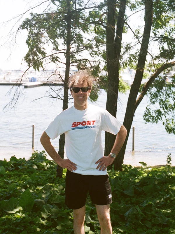 Man standing in Sport Design white shirt with trees in background.