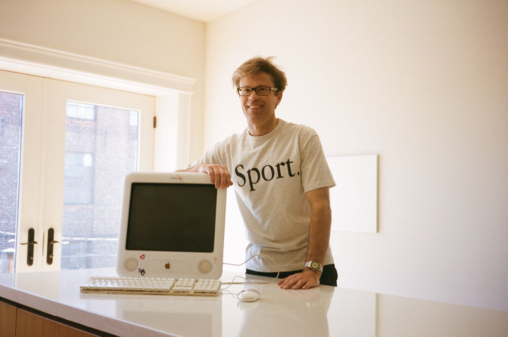 man standing in Sport shirt and early 2000s Mac computer